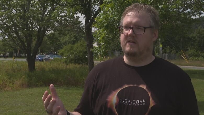 A man in classes gestures while speaking about eclipses on a warm summer day.