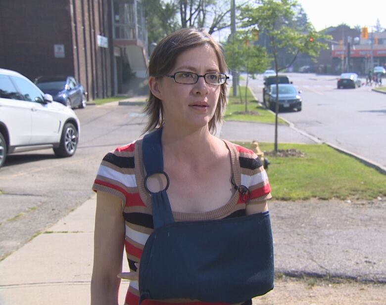 A woman with glasses stands with a sling on her left arm. 