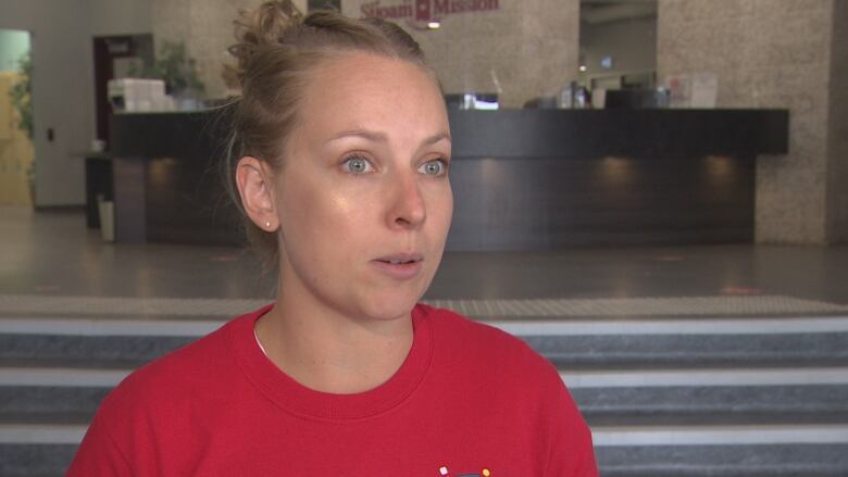 A woman in a red T-shirt speaks to someone off-camera.