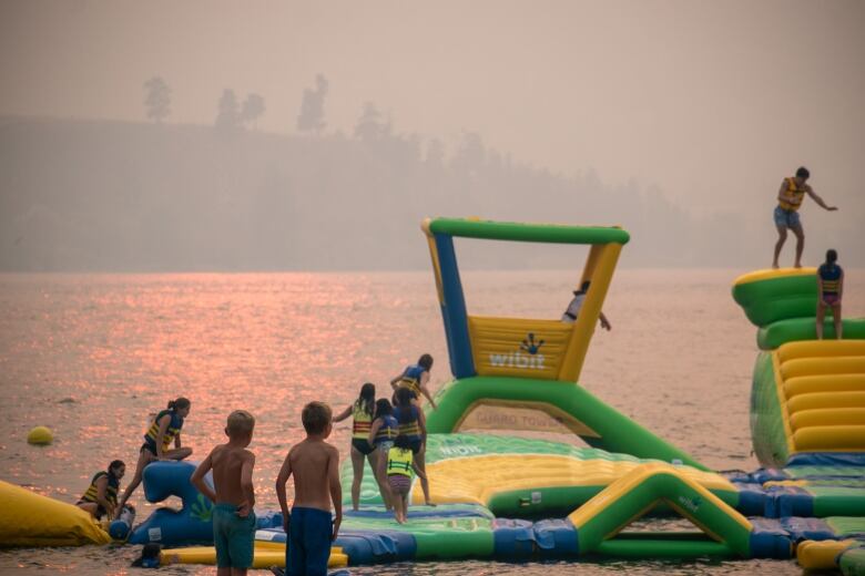 Children walk around and play on a beachside float installation, as wildfire smoke creates a hazy atmosphere.