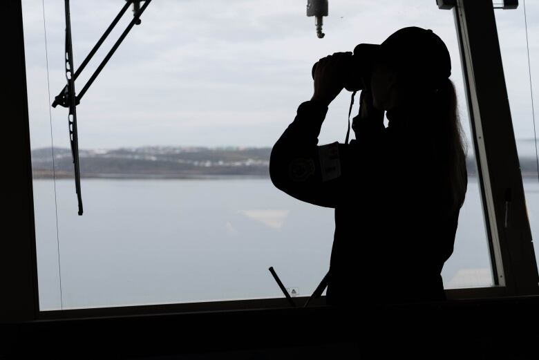 A woman looks through the front of the HMCS Harry Dewolf using binoculars in Iqaluit. 