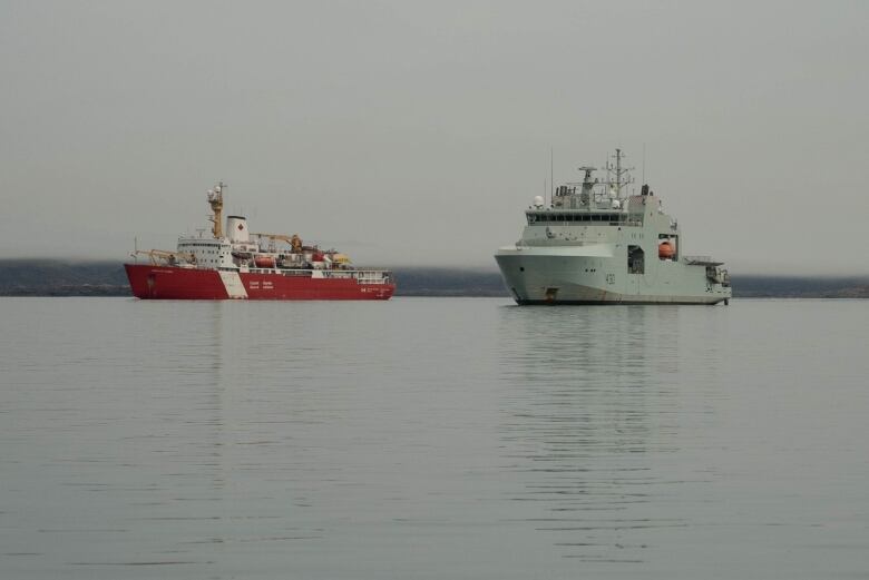 A red and white Canadian Coast Guard ship sits next to the HMCS Harry DeWolf in the water outside Iqaluit, Nunavut. 