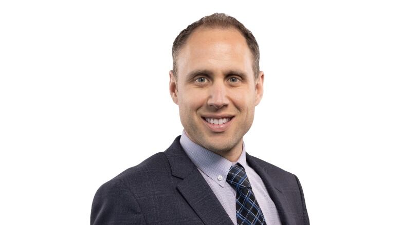 A man poses for a portrait against a white background and wears a suit.