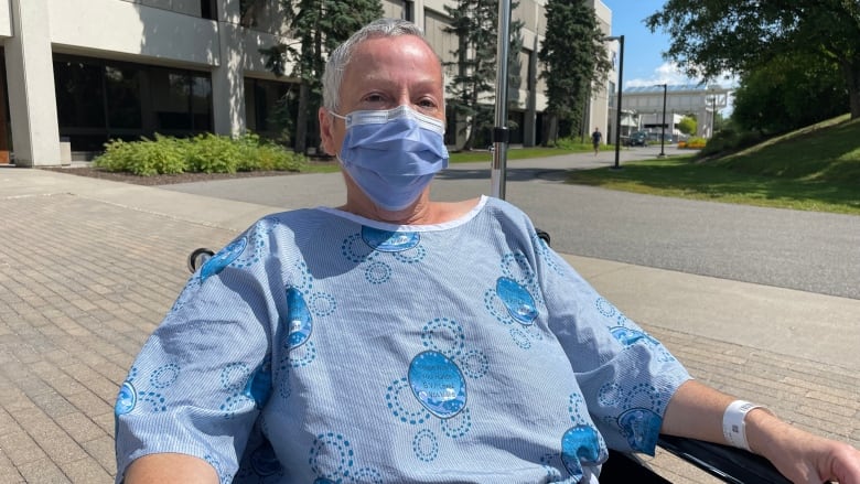 A hospital patient sits outside in a gown and face mask.