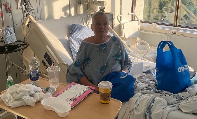 A hospital patient in a hospital room. A tray in front of her includes water and a coffee cup.