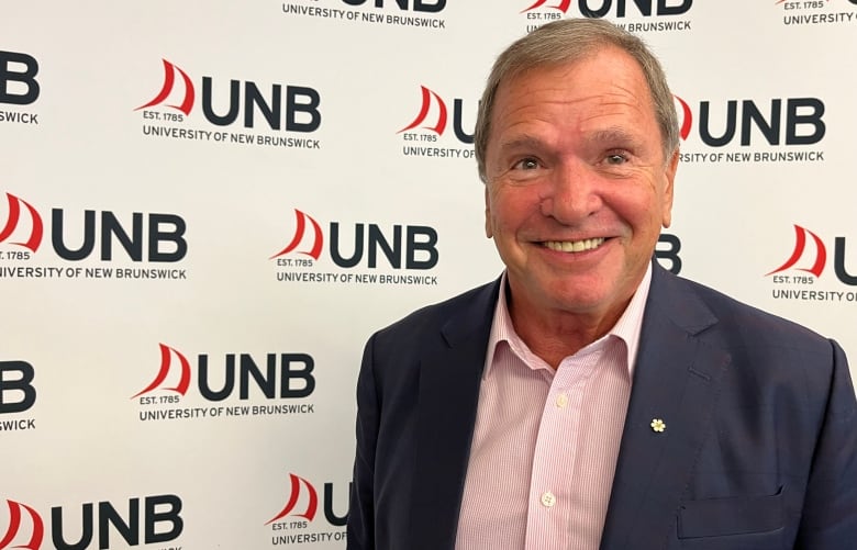 A smiling man in front of a background with the University of New Brunswick logo on it