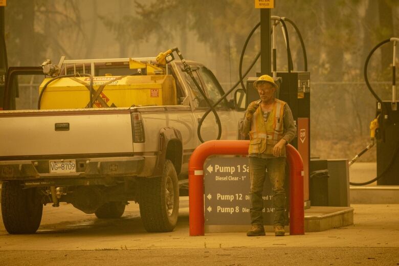 A man is pictured next to his truck at a gas station, amid a hazy yellow tint. 