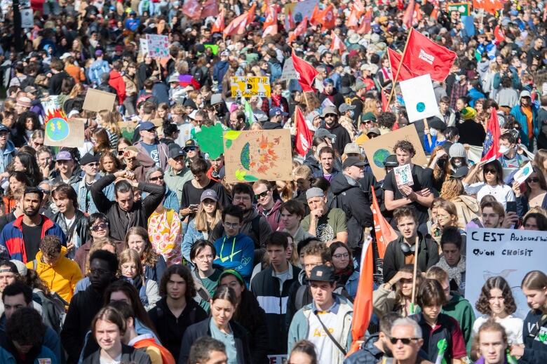 A large group of people, many carrying signs and flags, are shown on a Montreal street.