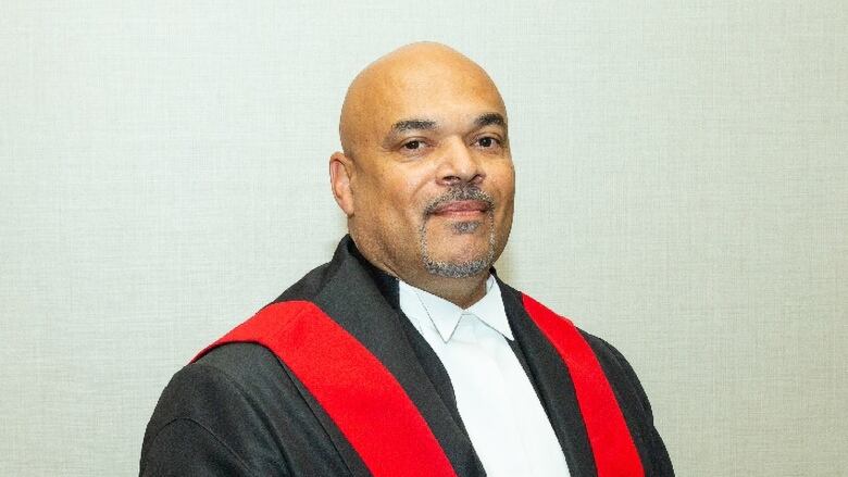 A man is shown wearing black and red judge's robes.