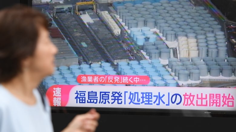 A woman watches a TV screen showing a news report on the release of the treated radioactive water from the Fukushima Daiichi Nuclear Power Plant.