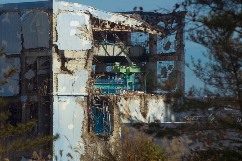 The exterior of a light blue building shows an exposed facade and extensive damage.