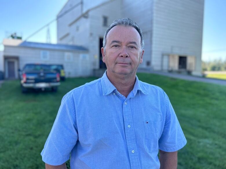 Older man in short-sleeved blue shirt stands in front of a grain elevator.