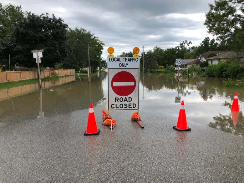 A road closure sign with a flooded street behind it.