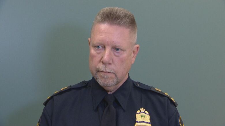 A man in a police uniform stands with a blank background