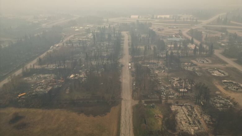 Drone aerial still of houses in Enterprise, N.W.T., burned by wildfire, with a smokey sky.