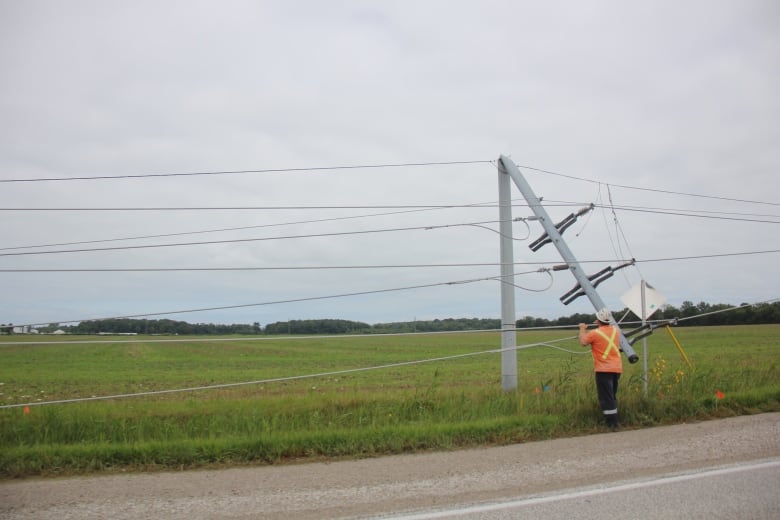 A power pole is bent in half while a worker stands at the base