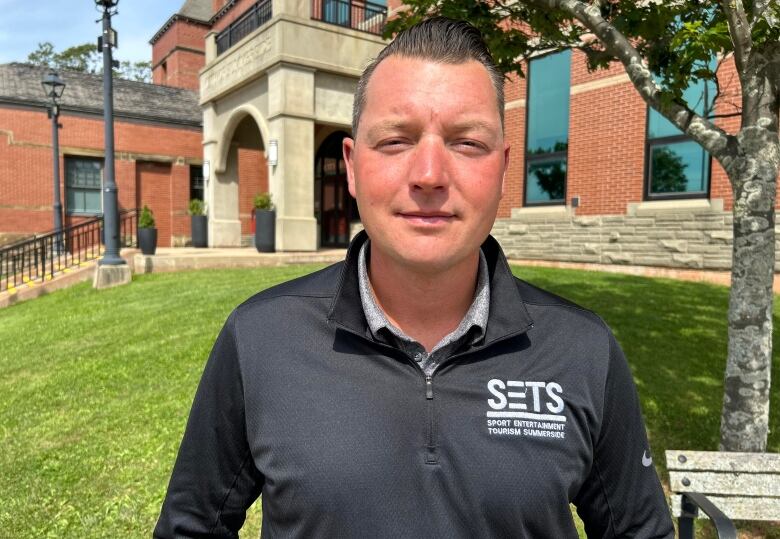 Man in zipped sweater stands in front of Summerside City Hall. 