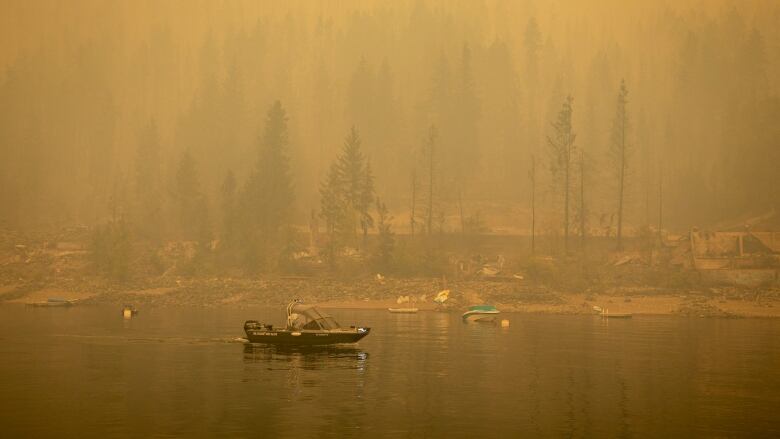 Homes destroyed with a boat on the water, heavy smoke.