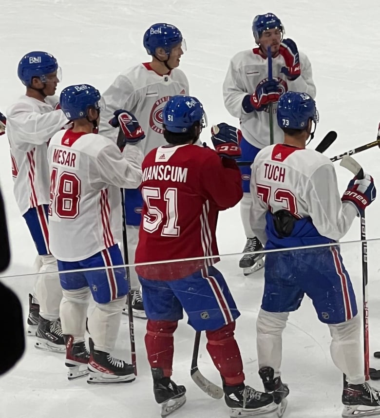 A group of hockey players stand in skates on the ice wearing the practice white and red hockey uniforms of the Montreal Canadiens.