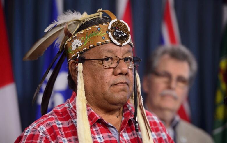 A man wearing a traditional Indigenous headdress speaks at a press conference.