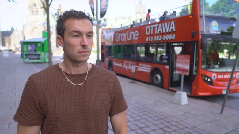 A man standing in front of a red double-decker bus.