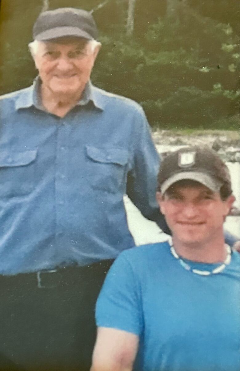 Two men side by side wearing blue shirts and black ball caps, smiling.