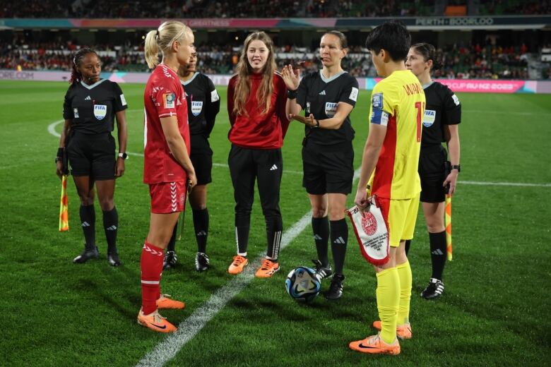 A soccer referee wearing black is tossing the coin on the field between two players before a Women's World Cup match between Denmark and China.