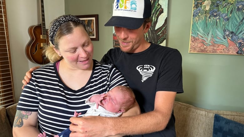 The mother and father of a newborn baby hold their child in their home.