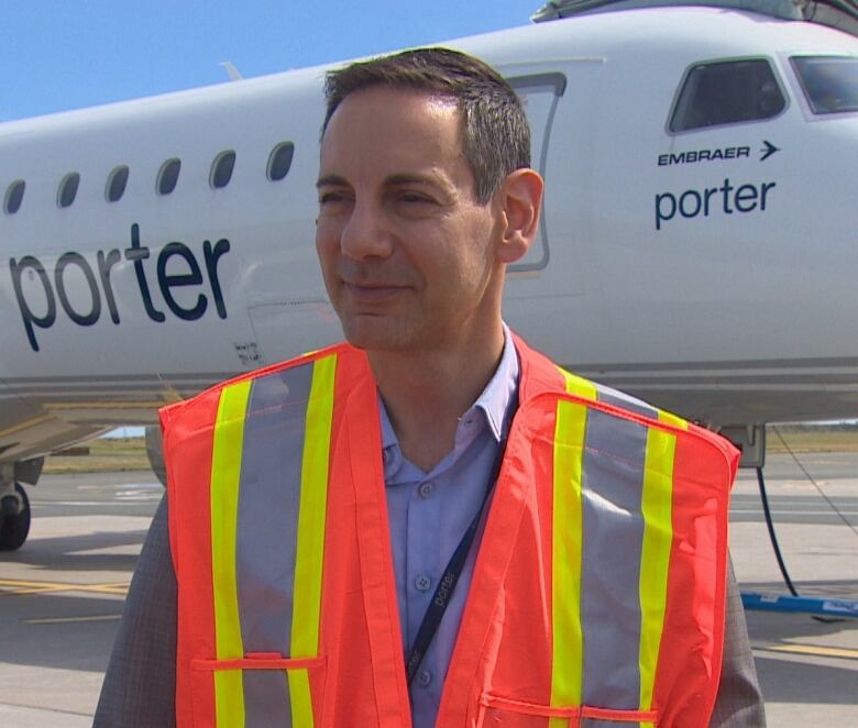 A middle-aged man smiles. He stands in front of a plane that says 