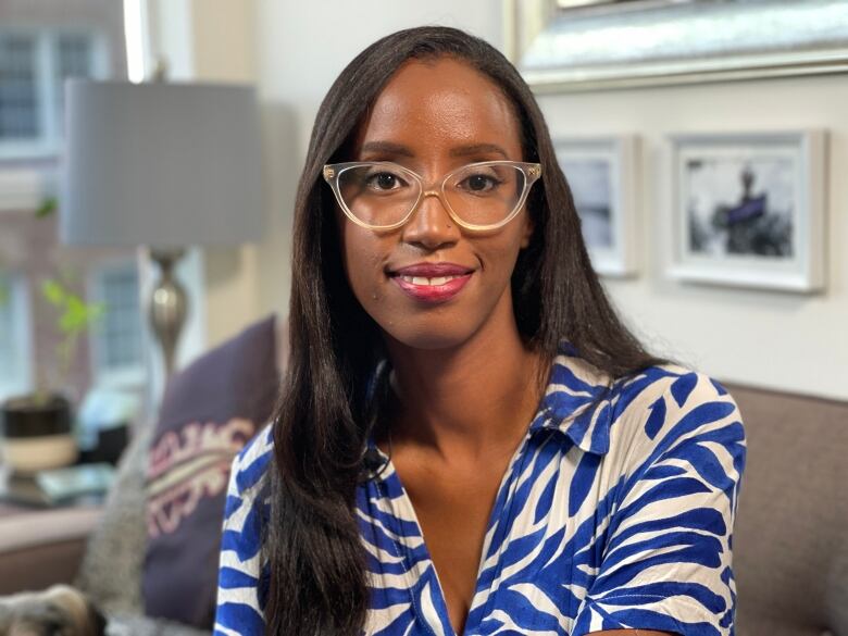 A woman wearing glasses and a blouse with a blue pattern smiles.