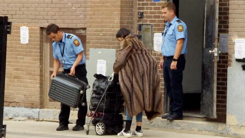 A woman in a coat stands behind a cart loaded with filled plastic bags.