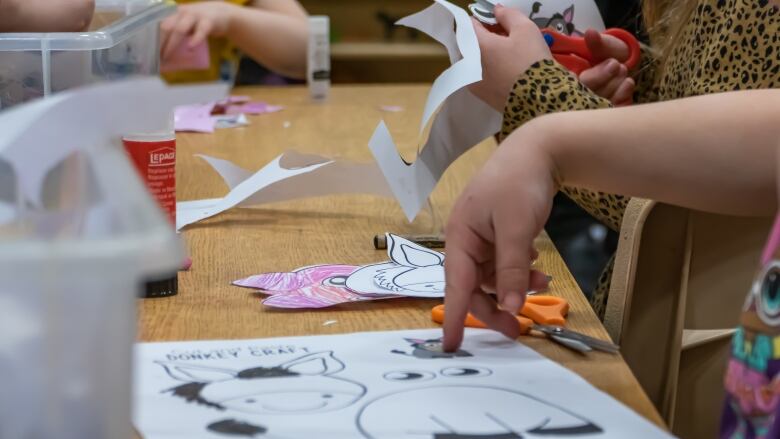 A closeup shows a child's hand pointing to a drawing of cartoon animals on a table, while other children are seen in the background working on crafts.