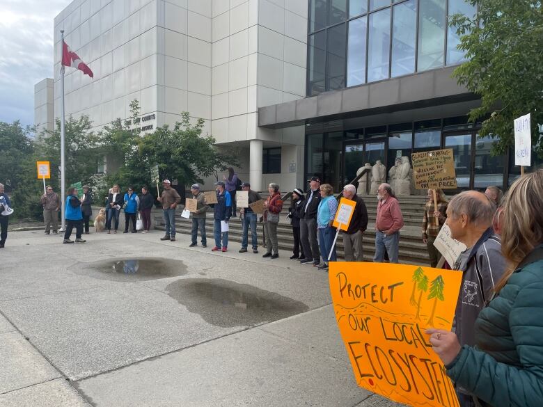 A group of a few dozen people stand with signs outside a courthouse on a grey afternoon.