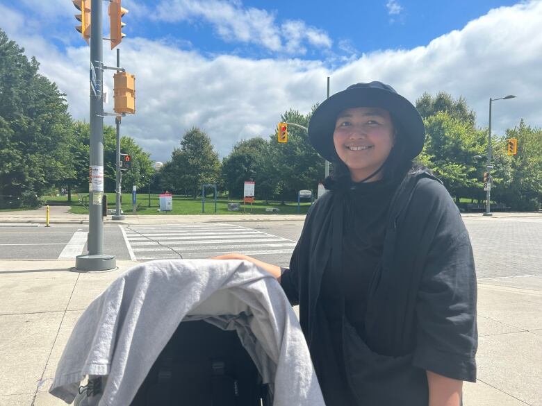 A woman beside a stroller looks into the camera for a photo.