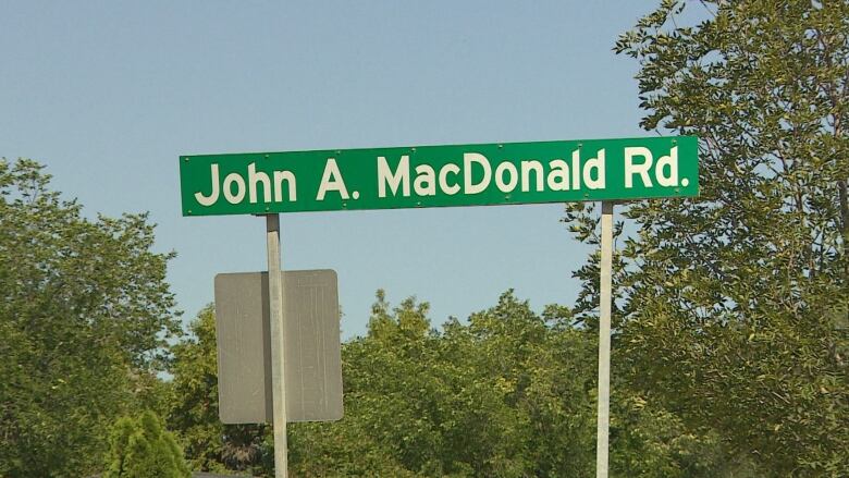 a green road sign of John A MacDonald Road with blue sky behind it