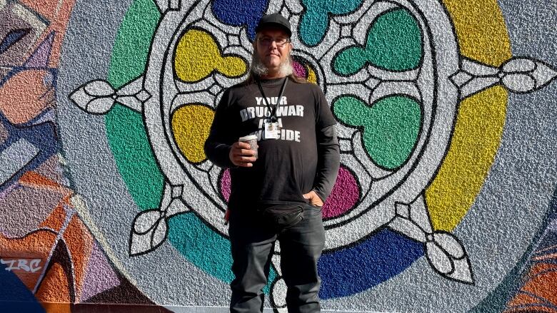 A man holding a coffee and wearing a shirt that says 