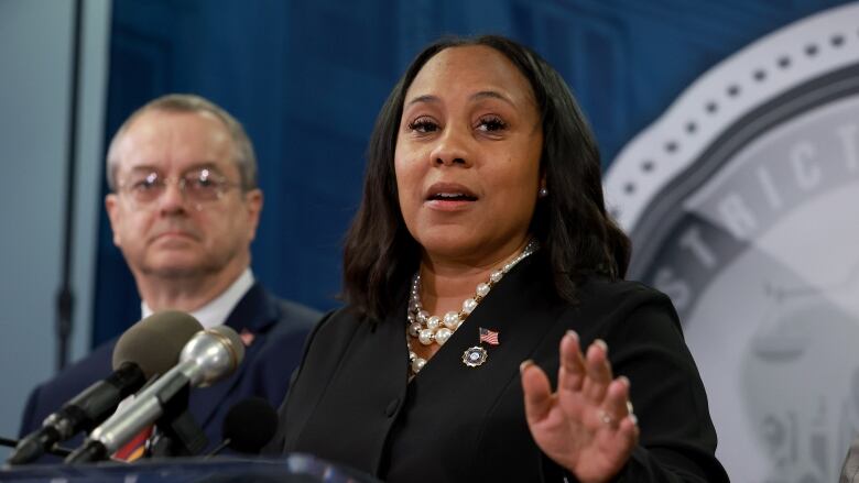 A woman in professional attire is shown speaking at a podium.