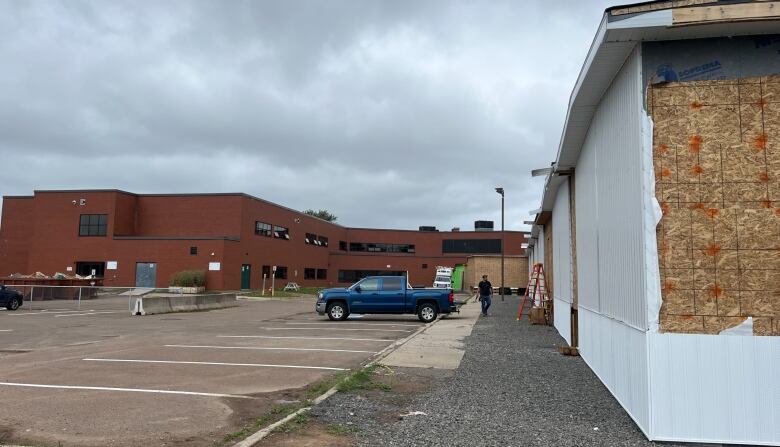 A two-storey brick school in the background with smaller structures on the right side with exposed plywood.