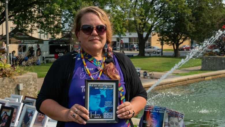 A woman stands in front of a water fountain while holding a photograph.