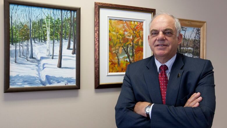 A man in a suit and tie stands in front of a portrait.