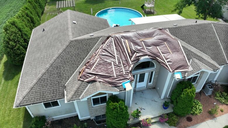 An aerial shot of a home with roof damage covered by tarps.