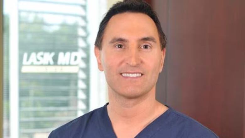 A man wearing blue scrubs stands in front of a LASIK MD office.