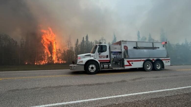 A fire truck next to flames on a highway.