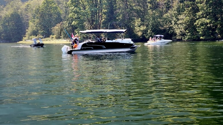 three boats are seen in front of a forested shore