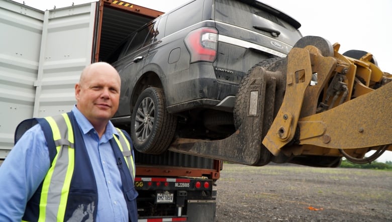 A man in a safety vest watches as a forklift unloads a stolen car from a shipping container. 