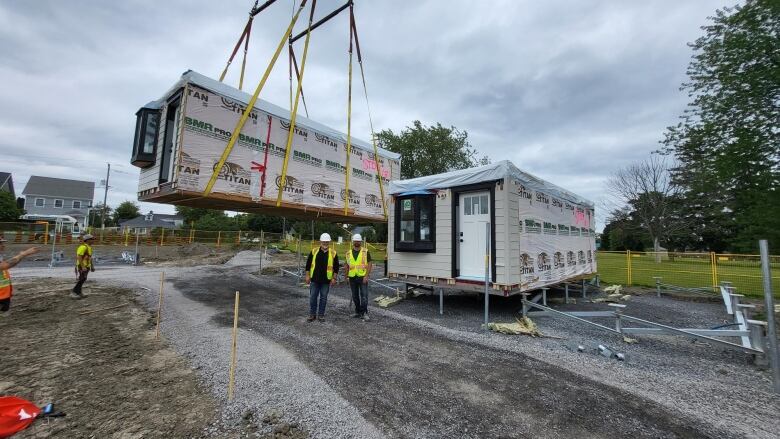 A crane lifts a home into a construction site on a cloudy day