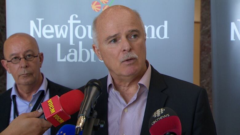 A man wearing a suit stands in front of three microphones.