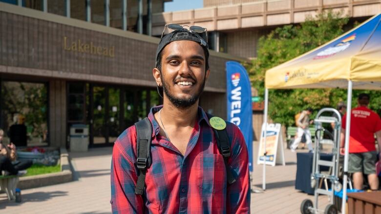 A man wearing a red and blue plaid shirt stands outside, smiling.