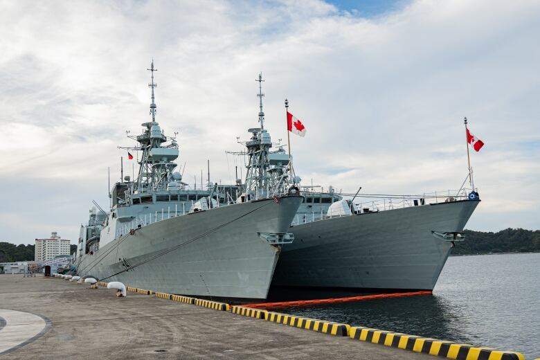 Two naval vessels sit moored next a dock.