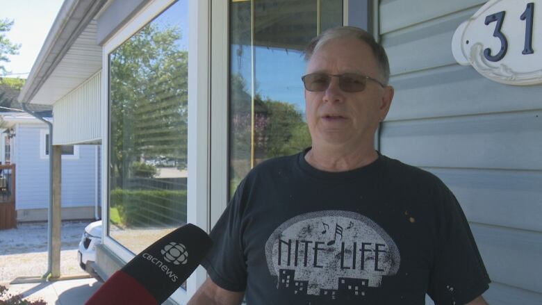 A man in a black t-shirt in front of a blue house. 